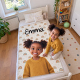 Mädchen kniet auf ihrem Bett neben der personalisierten 3D Decke mit dem Namen Emma und Regenbogenmuster